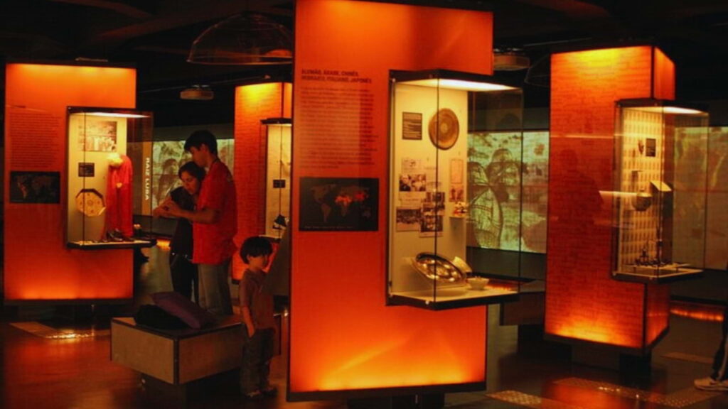 Visitantes interagindo com a exposição permanente do Museu da Língua Portuguesa, com painéis iluminados e recursos audiovisuais.