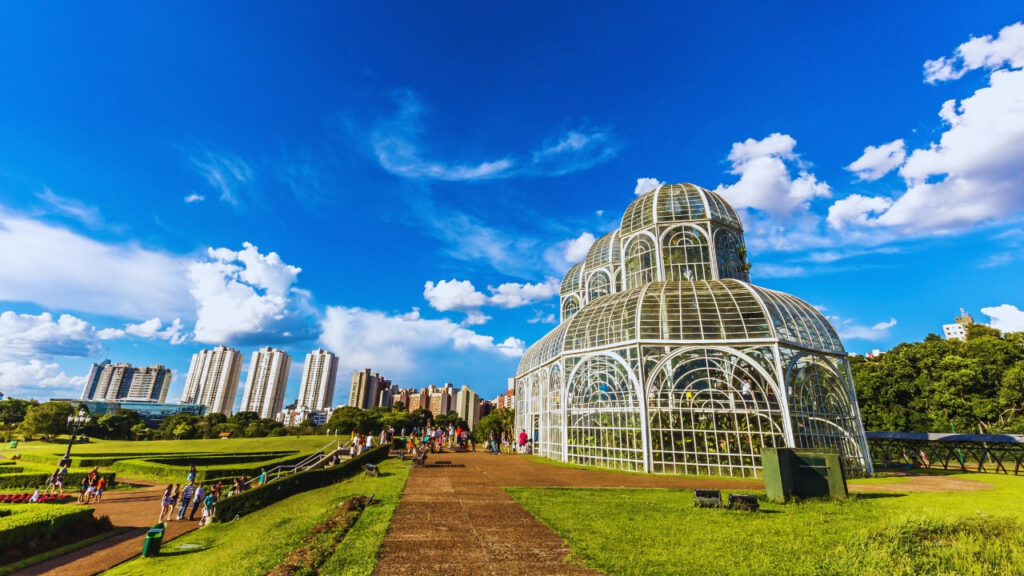 Imagem da estufa de vidro do Jardim Botânico de Curitiba com jardins e visitantes