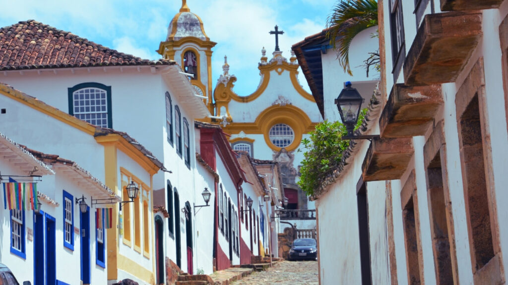 Rua de paralelepípedo típica de Ouro Preto com casas coloniais e uma igreja histórica ao fundo.