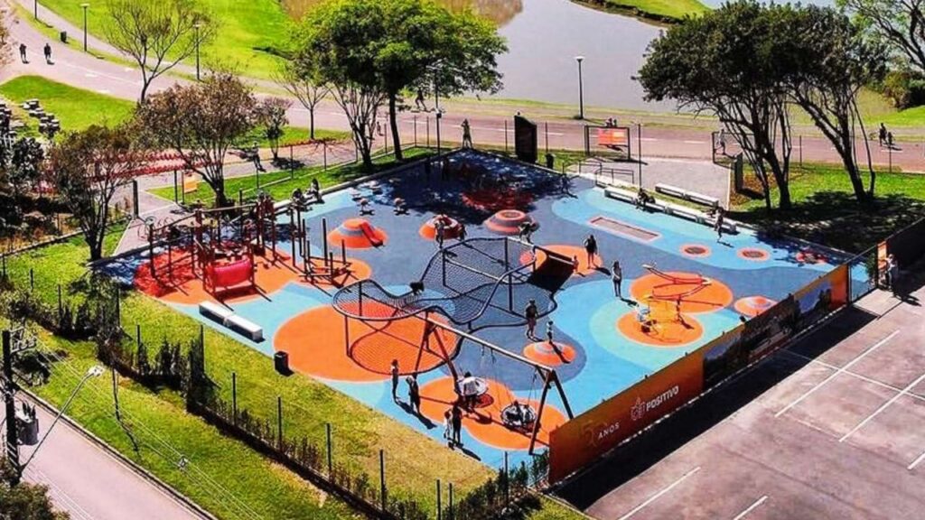 Parquinho infantil moderno no Parque Barigui, com brinquedos coloridos e área cercada, próximo ao lago e à ciclovia.
