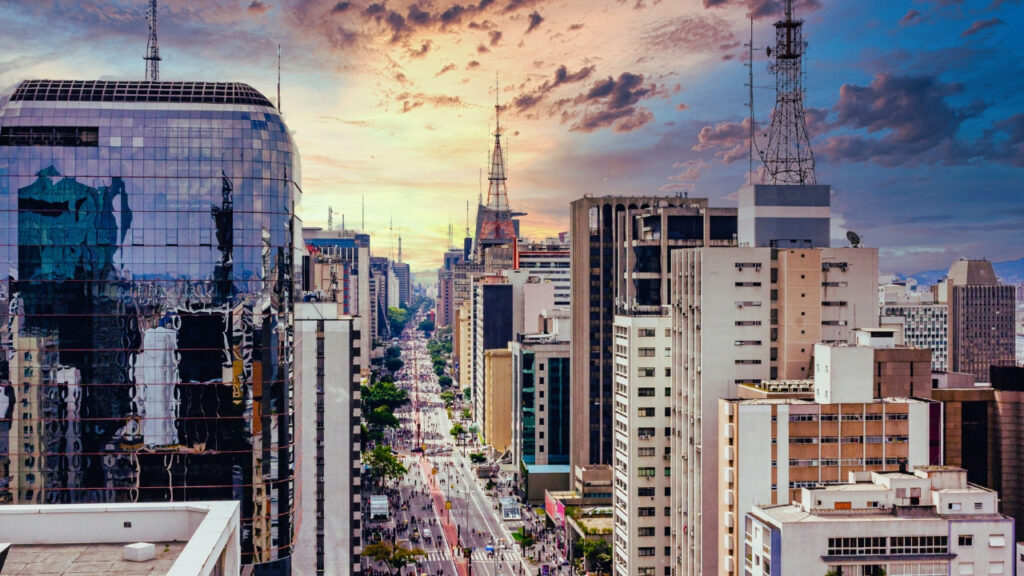 Vista da Avenida Paulista com prédios modernos, fluxo de carros e o clima urbano característico da cidade.