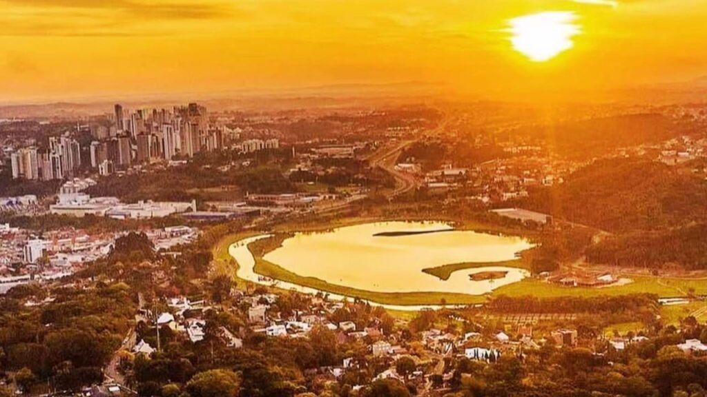 Vista aérea do Parque Barigui ao entardecer, com o lago em destaque.