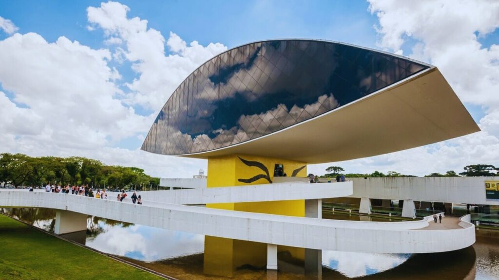 Museu Oscar Niemeyer em Curitiba, com arquitetura icônica em formato de olho e visitantes na passarela.