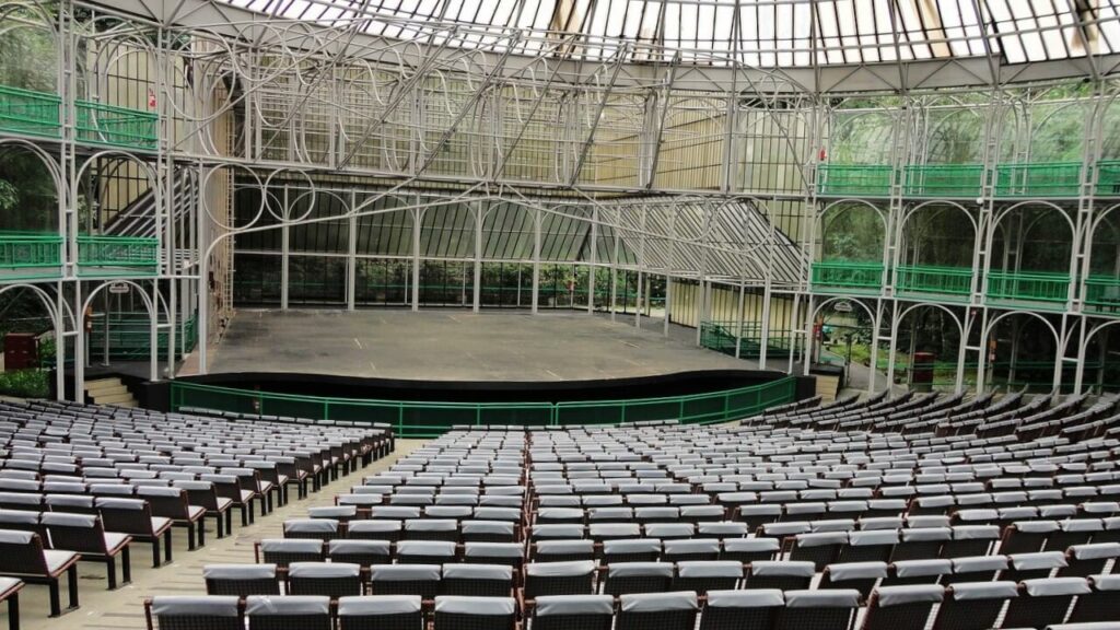 Interior da Ópera de Arame em Curitiba, com cadeiras organizadas e palco coberto, pronta para apresentações.