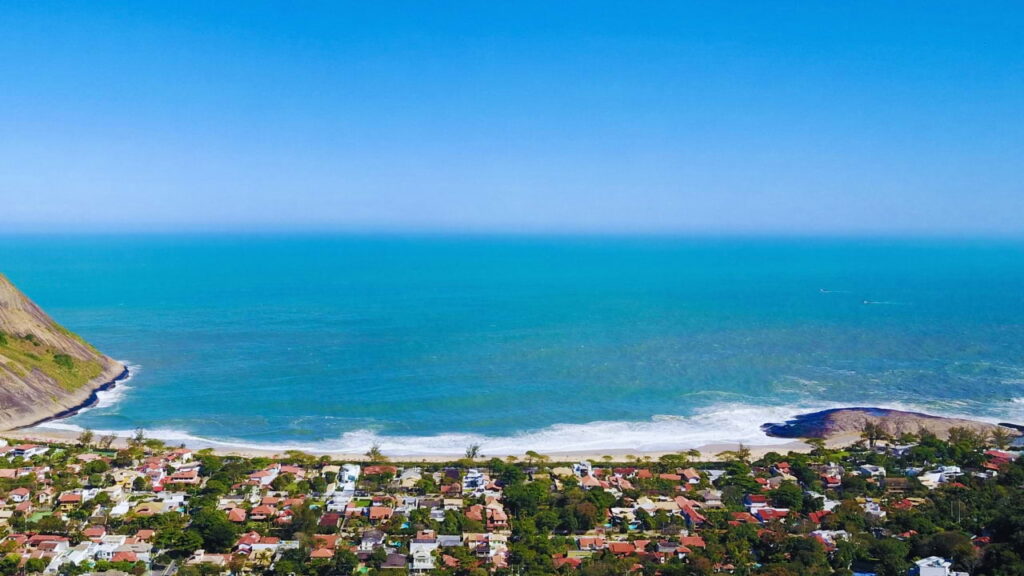 Vista aérea da Praia de Itacoatiara em Niterói, com mar azul e casas na orla.