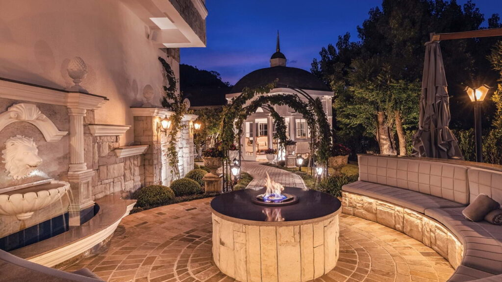 Área externa do hotem Colline de France em Gramado com firepit aceso e jardim iluminado à noite.