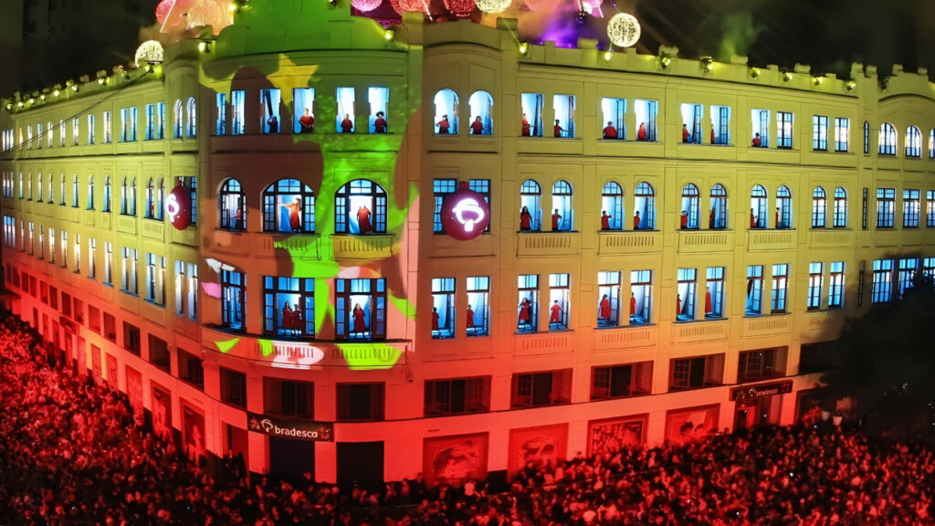 Apresentação do Coral do Palácio Avenida em Curitiba, com janelas iluminadas e grande público reunido na Rua das Flores durante o Natal do Bradesco.
