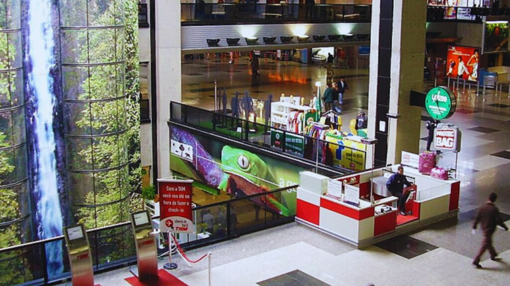 Interior do Aeroporto Internacional Afonso Pena com painéis decorativos que retratam a natureza paranaense e lojas de conveniência.