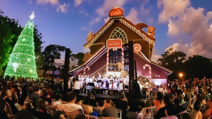 Público reunido no Bosque Alemão, em Curitiba, assistindo a espetáculo natalino ao ar livre com casa temática iluminada e grande árvore de Natal verde.