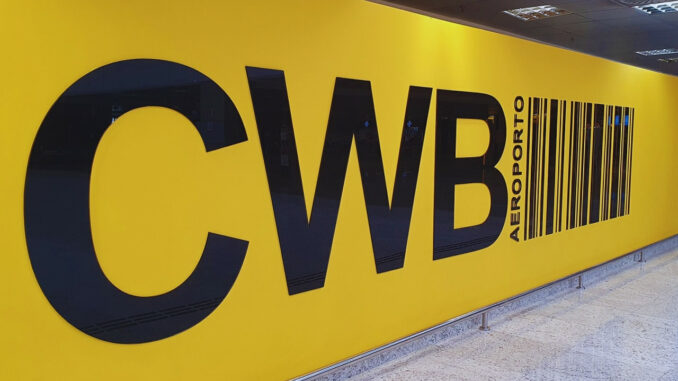 Painel amarelo com as letras CWB em destaque na área interna do Aeroporto Internacional Afonso Pena, em Curitiba.