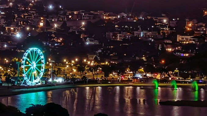 Roda-gigante iluminada no Parque Barigui à noite, refletida no lago, com as luzes da cidade ao fundo em Curitiba.