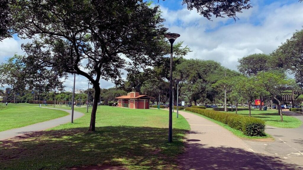 Pistas de caminhada do Parque Barigui em meio ao gramado e árvores, com estrutura de banheiros ao fundo.