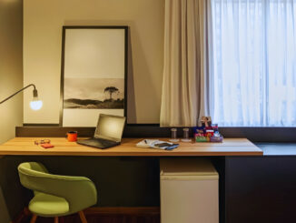 Quarto de hotel em Curitiba com luminária acesa, notebook sobre a mesa e ambiente iluminado, ilustrando o uso da voltagem de 110 volts na cidade.