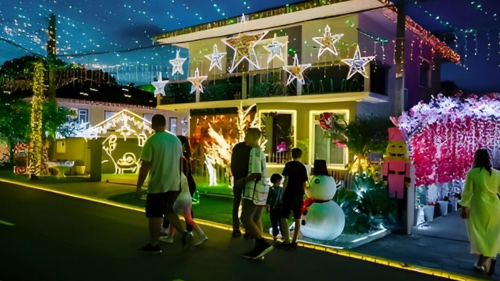 Famílias caminhando pela Rua Iluminada Família Moletta, em Curitiba, com casas decoradas com luzes de Natal.